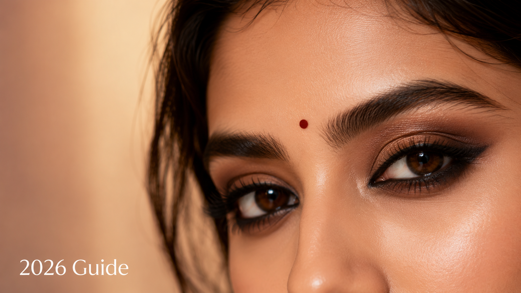 Close-up of a woman's face highlighting her striking eye makeup, featuring bold eyeliner and warm eyeshadow tones, complemented by a subtle bindi and glowing skin, suitable for Indian skin tones.